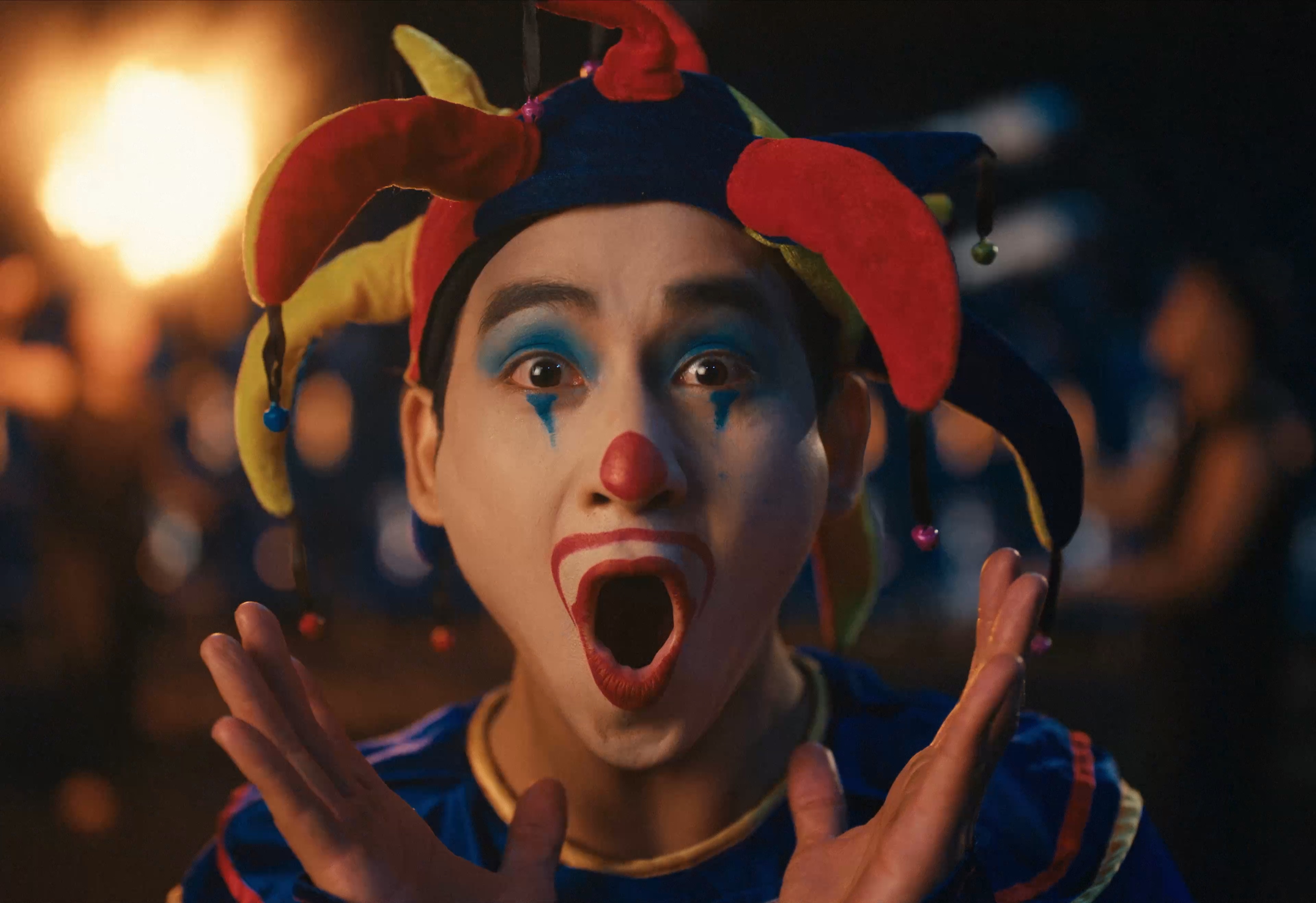 Close-up of a performer in a colorful jester costume under warm stage lighting